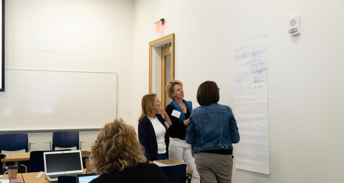 three people stand and look at a large sheet of paper with writing