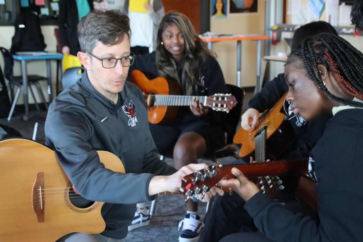 A guitar teacher shows a teen student a fingering