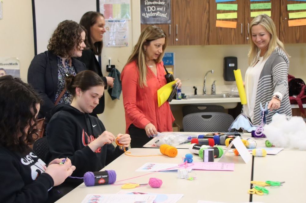 Four adults watch two teens make a craft with yarn