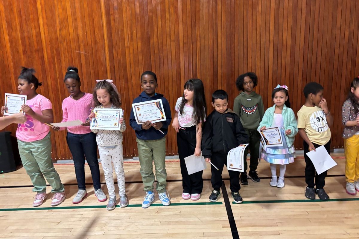 Children stand in a row at an elementary school holding certificates