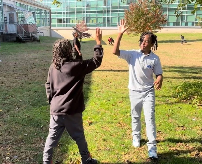Two students at East Hartford Middle School give each other a high five in the school yard as others look on (Laura Roberts/East Hartford Public Schools) 